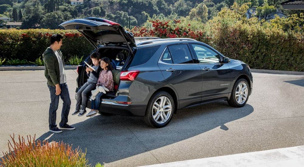 A father is next to a grey 2021 Chevy Equinox while two kids sit in the open liftgate. 
