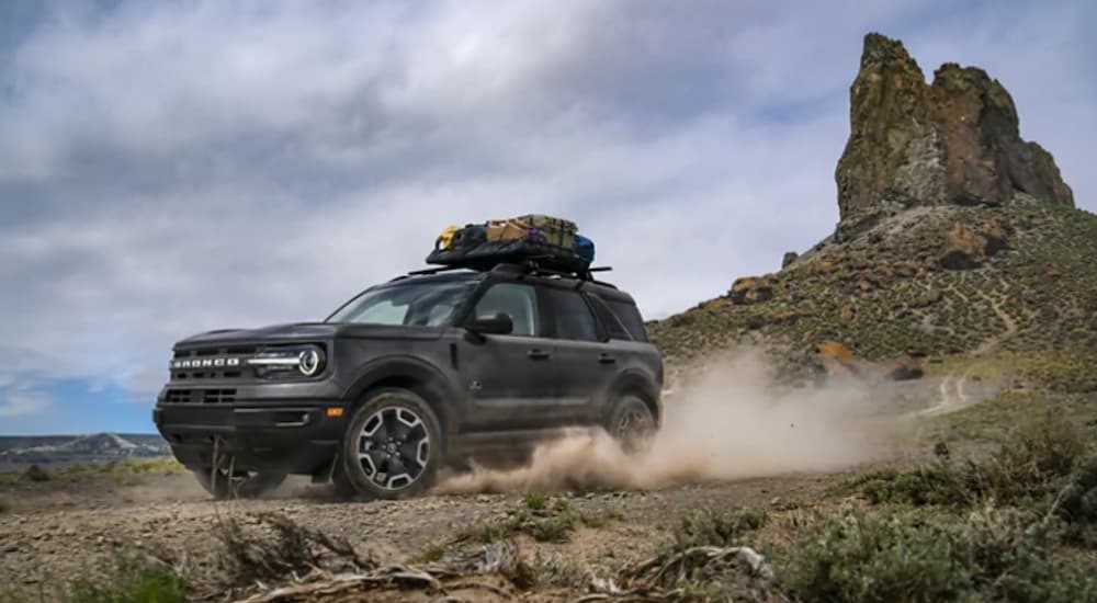 A Grey 2021 Ford Bronco Sport drives in a desert with rock formation behind it. 