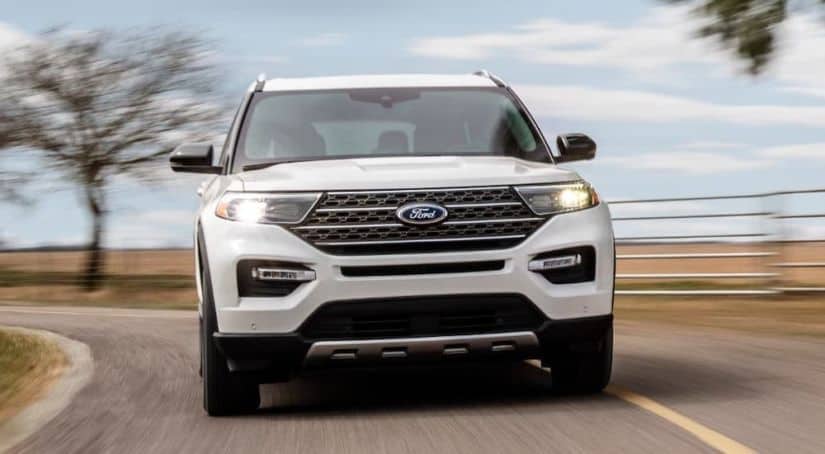 A white 2021 Ford Explorer King Ranch is shown from the front driving on a road in front of yellow grass and a tree.