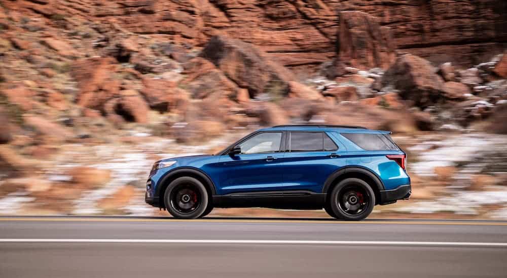 A blue 2021 Ford Explorer ST is shown from the side driving in front of a rock face.