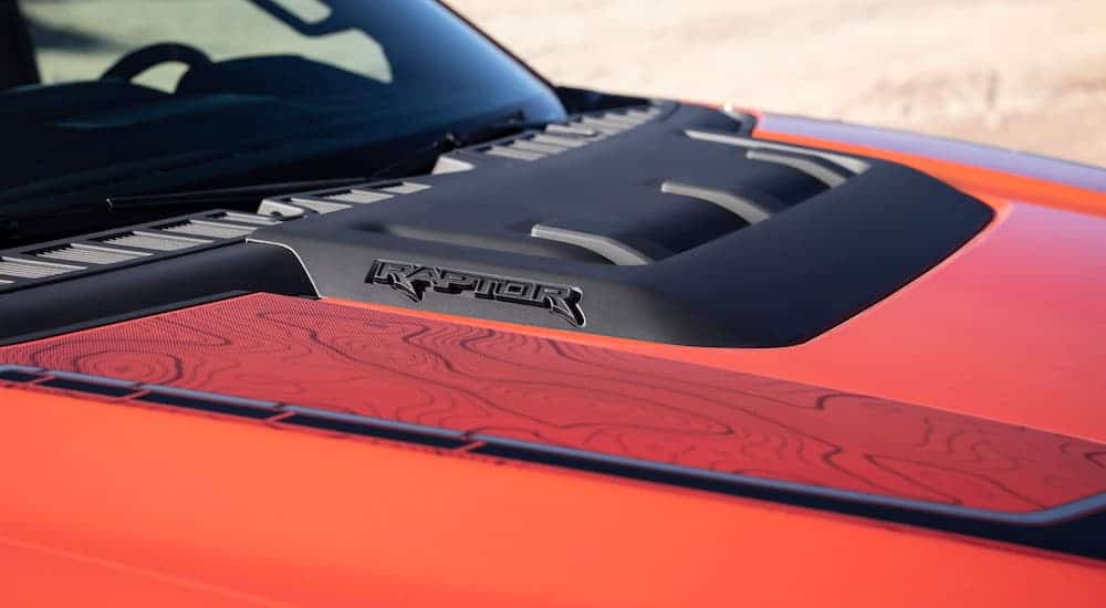 A close up shows the vented hood and Raptor logo on a red 2021 Ford F-150 Raptor.