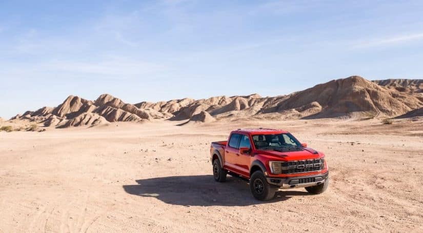 A red 2021 Ford F-150 Raptor is shown from the front parked in a desert.