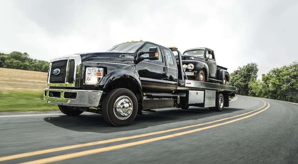 A black 2021 Ford F-650 Tow Truck is hauling a black 1950s Ford truck.