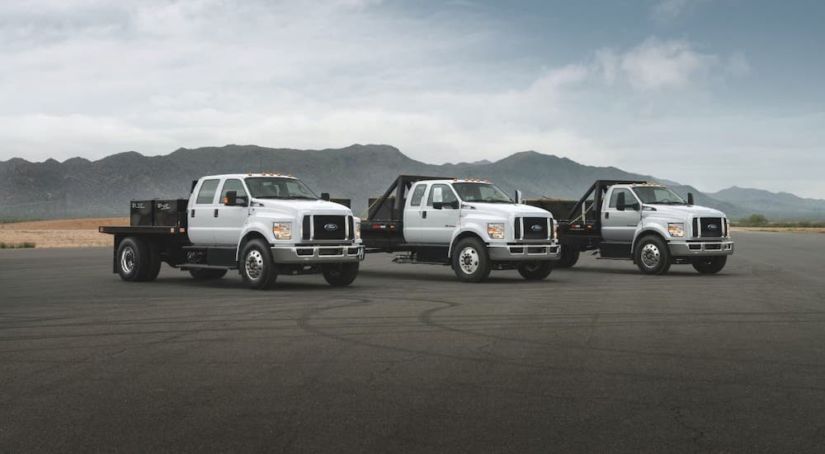Three white chassis cab Ford F-650 and F-750 trucks are parked in an empty lot in front of mountains as part of the 2021 Ford F-650 vs 2021 Ford F-750 comparison.