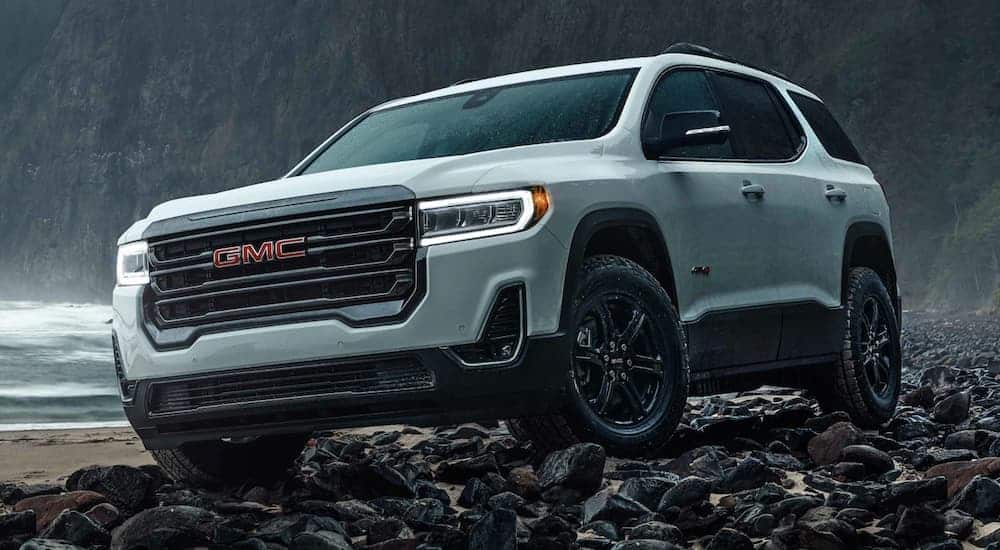 A white 2021 GMC Acadia AT4 is parked on a rocky shore in the rain.