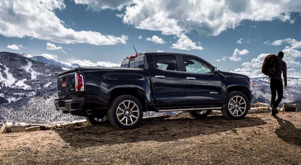 A black 2021 GMC Canyon is shown from the side parked next to someone hiking.