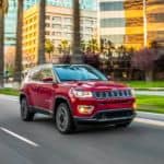 A red 2021 Jeep Compass is driving on a city street.