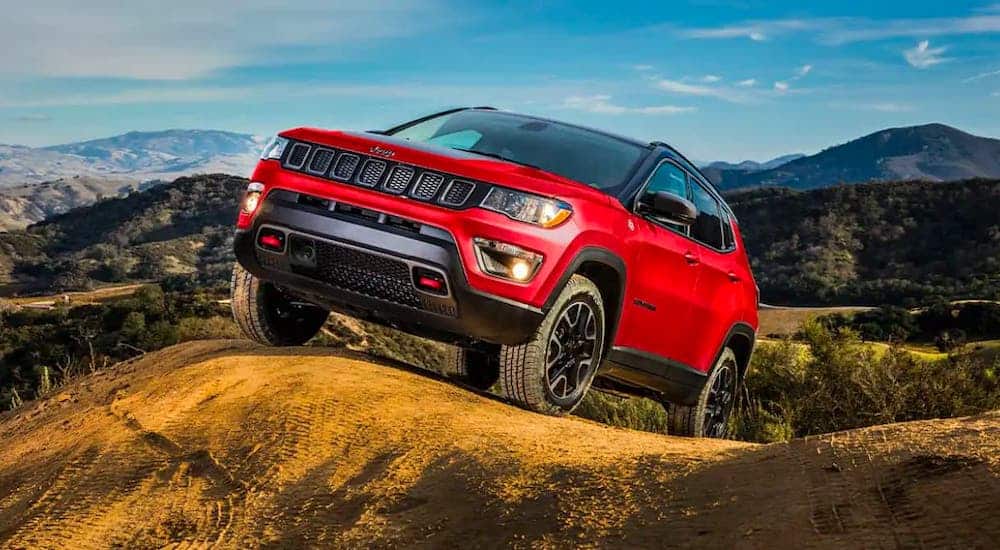 A red 2021 Jeep Compass Trailhawk is driving on a dirt trail.