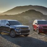 A red and a gray 2021 Jeep Grand Cherokee L is parked in front of distant mountains.