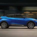 A blue 2021 Nissan Kicks drives through an urban area.