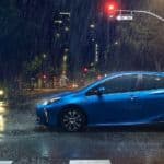 A blue 2021 Toyota Prius is shown from the side driving in a city in the rain at night.