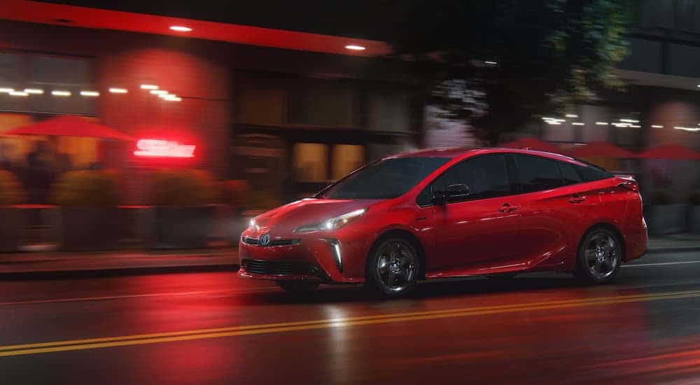 A red 2021 Toyota Prius is driving on a city street at night after winning the 2021 Toyota Prius vs 2021 Honda Insight comparison.