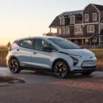 A pale blue 2022 Chevy Bolt EV is parked in front of a beach house.