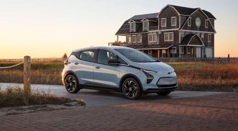 A pale blue 2022 Chevy Bolt EV is parked in front of a beach house.