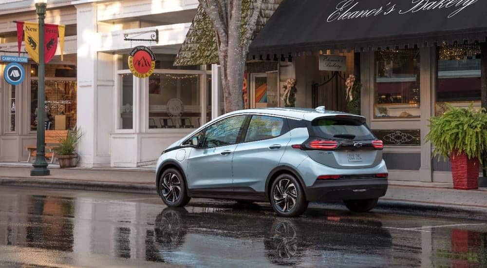 A pale blue 2022 Chevy Bolt EV is parked in front of shops.