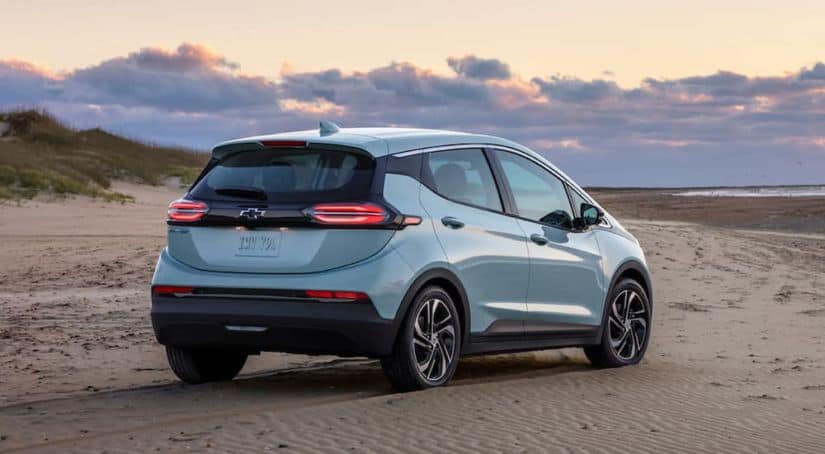 A light blue 2022 Chevy Bolt EV is shown form the rear on a beach at sunset.