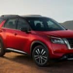 A red 2022 Nissan Pathfinder is parked on dirt in front of mountains.