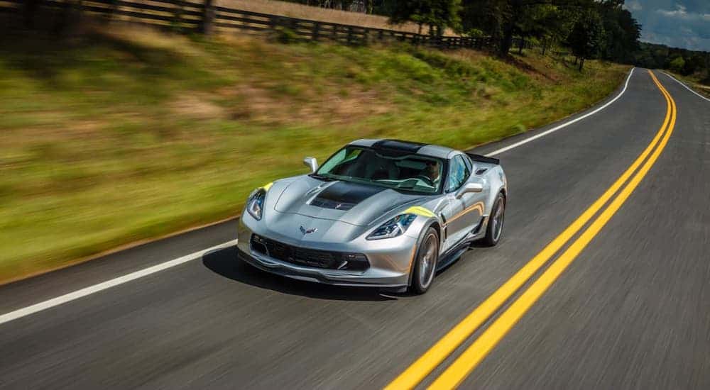 A silver 2017 Chevy Corvette is driving on a road.