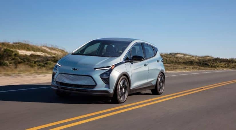 A pale blue 2022 Chevy Bolt EV is driving on a highway after leaving a local Chevy dealership.