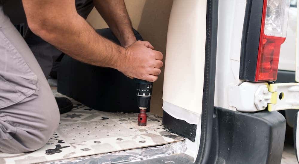 A closeup shows someone drilling the floor on a white commercial vehicle.