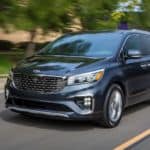 A grey 2021 Kia Sedona is shown driving down an empty road.