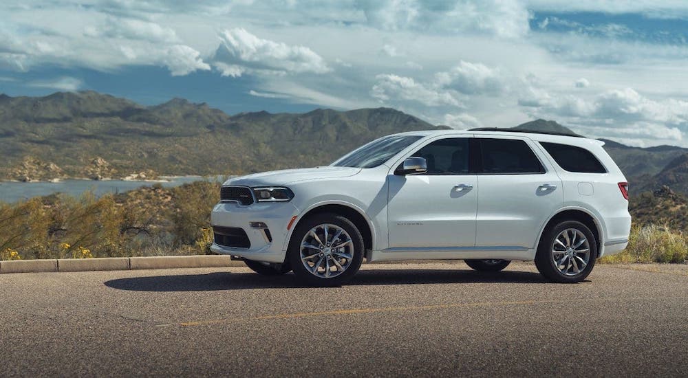A white 2021 Dodge Durango is shown from the side on a highway in front of a river and mountains.
