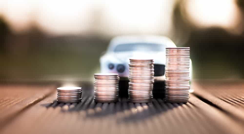 An increasing set of coins is shown with a blurred car in the background.