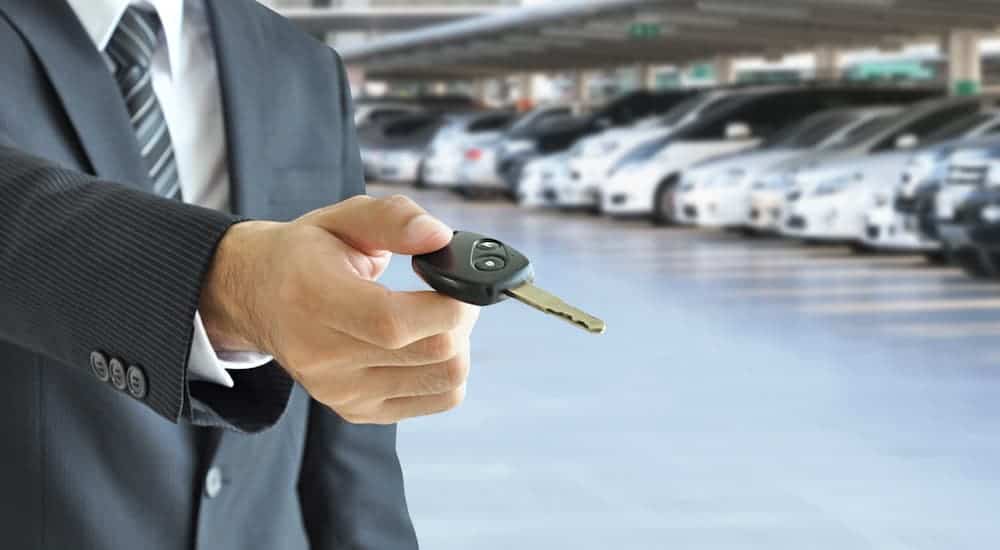 A salesman is holding out a set of car keys at a dealership that offers Ford leases in Louisville.