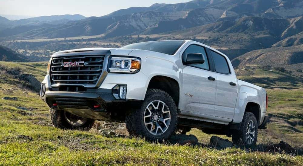 A white 2021 GMC Canyon from a GMC dealership is off-roading on a grassy mountainside.