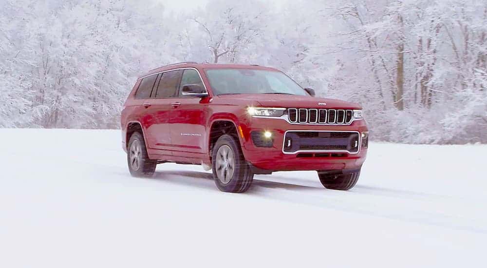 A red 2021 Jeep Grand Cherokee L is shown from the side while parked in the snow.