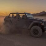 A black 2021 Jeep Wrangler Rubicon 392 with no roof is kicking up sand in a desert at sunset.
