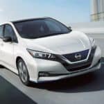 A white 2021 Nissan LEAF is driving on a highway overpass.