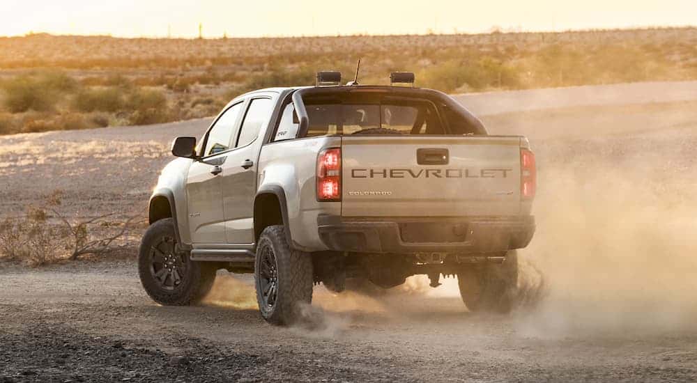 A tan 2021 Chevy Colorado ZR2 is shown from the rear parked on sand with dust in the air.