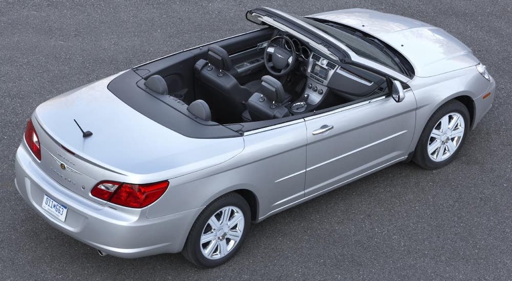 A silver 2010 Chrysler Sebring convertible with the top down is shown from a high angle in a parking lot.
