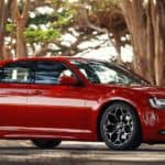 A great car to find at a pre-owned Chrysler dealer, a red 2016 Chrysler 300, is parked at an angle on a tree-lined road.