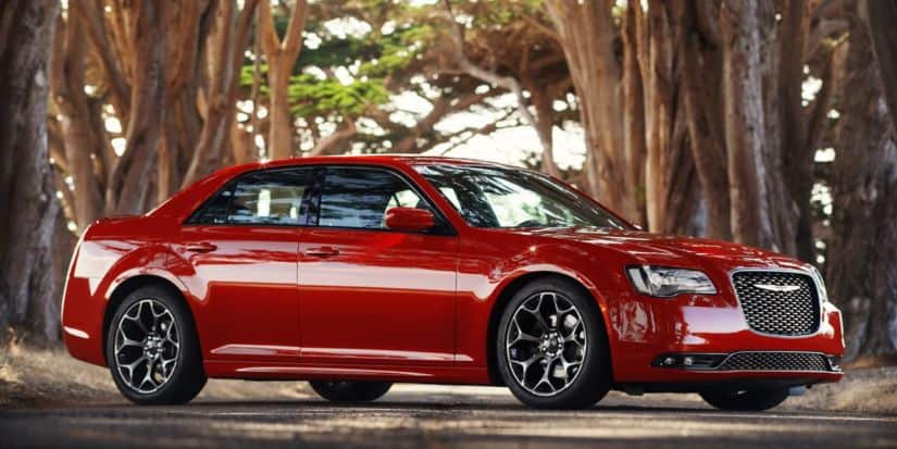 A great car to find at a pre-owned Chrysler dealer, a red 2016 Chrysler 300, is parked at an angle on a tree-lined road.