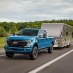 A blue 2020 Ford F-250 Super Duty Tremor is towing a trailer down the highway.