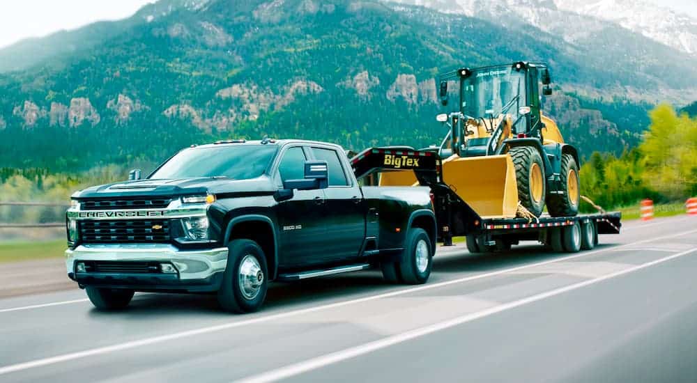 A black 2021 Chevy Silverado 3500HD is towing construction equipment on a gooseneck trailer.