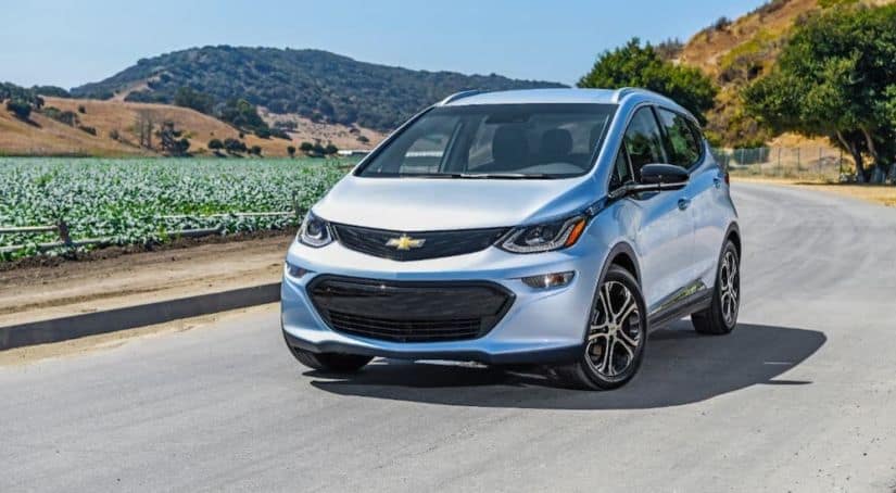 A silver 2018 Chevy Bolt EV is driving next to a farm.