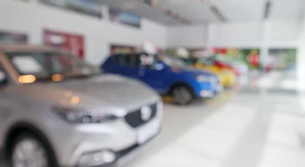 A row of blurred used cars is shown at a dealersip.