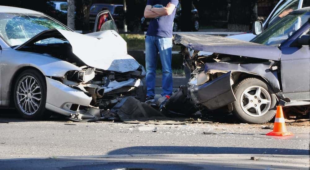 A man is shown standing between two cars after a collision.