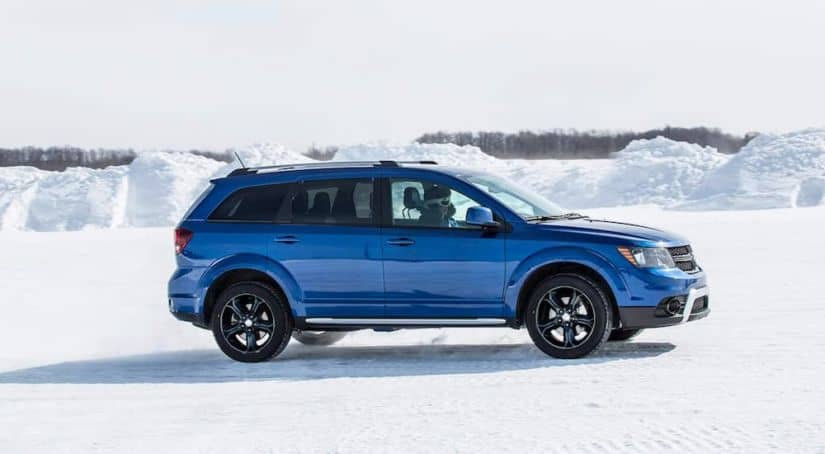 A blue 2020 used Dodge Journey is shown from the side driving through the snow.