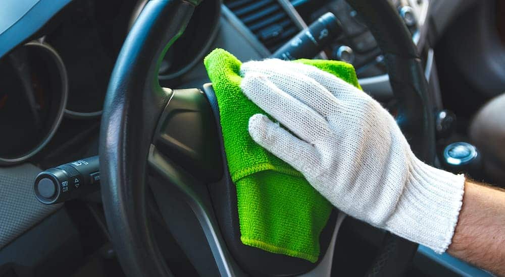 A close up shows a gloved hand wiping down a steering wheel with a microfiber towel.