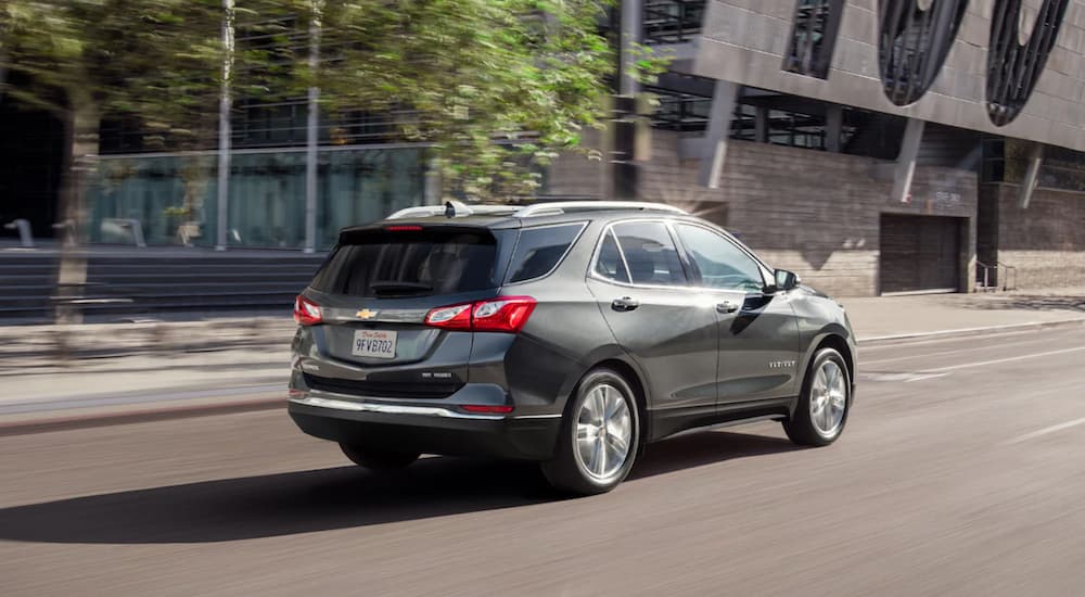 A silver 2021 Chevy Equinox shown from the back is driving through an urban area.