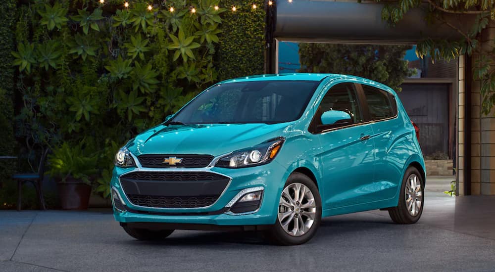 A turquoise 2021 Chevy Spark is parked next to a wall of plants.