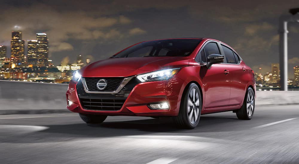 A red 2021 Nissan Versa is driving through a city at night.
