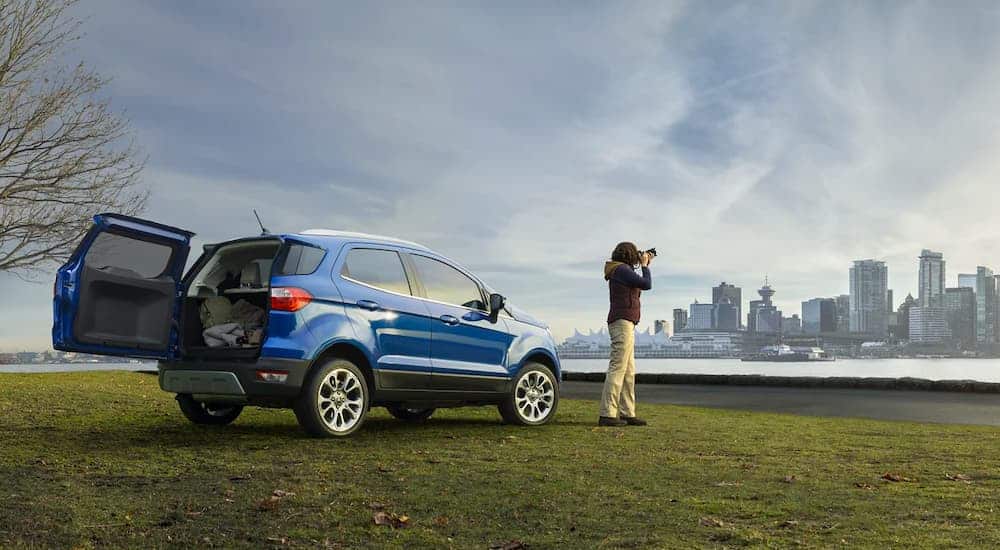 A blue 2021 Ford EcoSport is shown from the side next to a photographer, taking photos of a city, across a bay.
