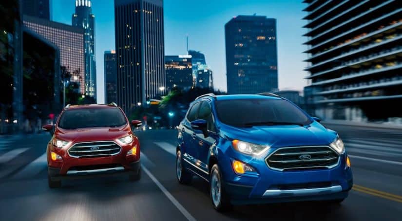 A red and a blue 2021 Ford EcoSport are driving next to each other down a city street at night.