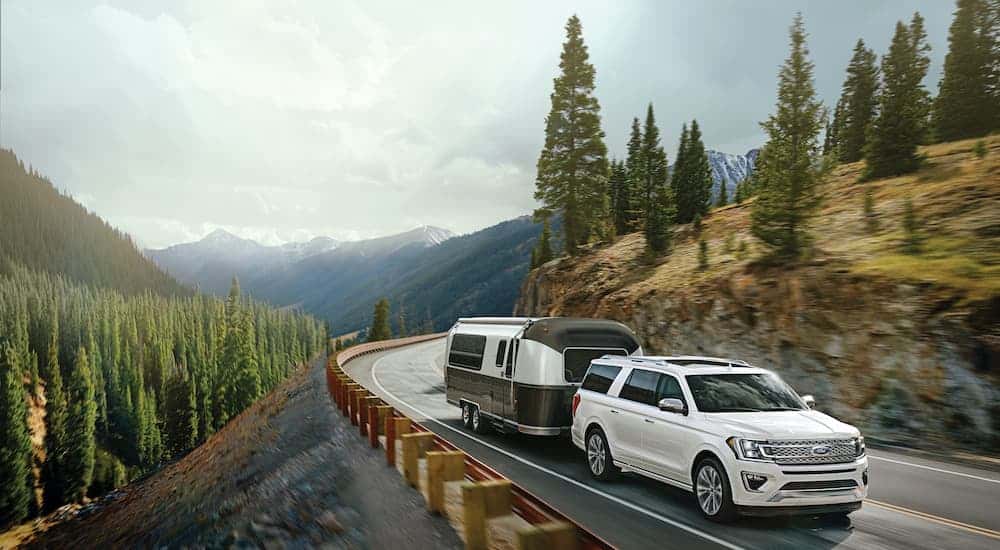 A white 2021 Ford Expedition Platinum Max is towing a trailer down a tree-line road.