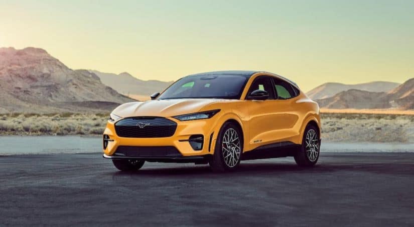 A yellow 2021 Ford Mustang Mach-E is parked in front of distant mountains.